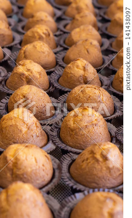 Rows of golden-brown baked muffins arranged in dark paper liners, fresh from oven, cooling on metal rack, delicious sweet pastry dessert, ready for consumption vertical photo 141438097