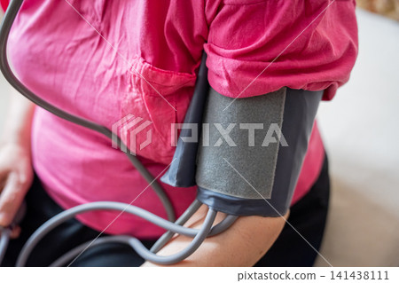 Close-up of adult wearing blood pressure cuff while monitoring health at home. Cardiovascular health management and preventive healthcare awareness Close-up of adult wearing blood pressure cuff while monitoring health at home. Cardiovascular health management and preventive healthcare awareness 141438111