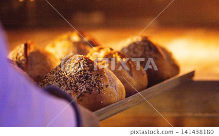 Artisan bread loaves with various seed topping on wooden peel, hand inserting into glowing hot oven, manual bakery production, fresh baked. Artisan bread loaves with various seed topping on wooden peel, hand inserting into glowing hot oven, manual bakery production, fresh baked. 141438180
