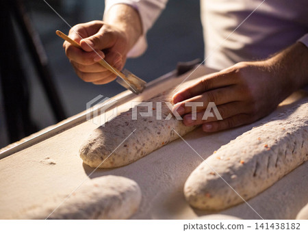 Baker hands preparing artisan bread dough loaves for baking on floured surface manufacturing process fresh bakery product production factory setting 141438182