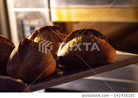Rustic bread loaves showing crispy crust texture, warm glow from oven highlighting artisanal baking process factory production. 141438183