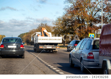 Rear view of multiple vehicles travelling on multi-lane road with autumn trees along roadside under partly cloudy sky day traffic scene transportation journey concept Rear view of multiple vehicles travelling on multi-lane road with autumn trees along roadside under partly cloudy sky day traffic scene transportation journey concept 141438288