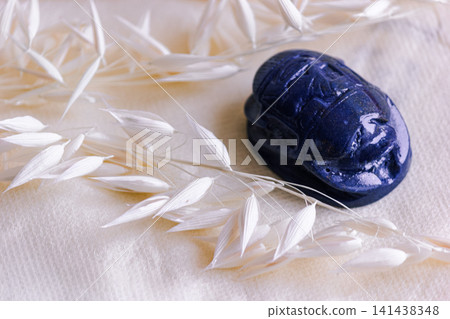 Carved blue lapis lazuli scarab amulet on beige linen fabric. 141438348