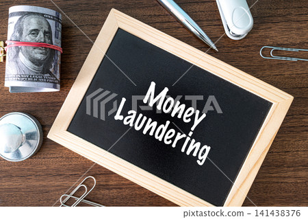 Money Laundering text on black chalkboard with dollar bills and office supplies on wooden desk, financial crime concept 141438376