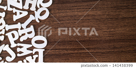 Few scattered white wooden letter tiles on empty dark brown wooden background, minimalist typography concept Few scattered white wooden letter tiles on empty dark brown wooden background, minimalist typography concept 141438399