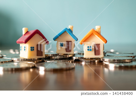 Three colorful miniature toy houses on pile of coins on blue background, real estate investment and mortgage concept Three colorful miniature toy houses on pile of coins on blue background, real estate investment and mortgage concept 141438400