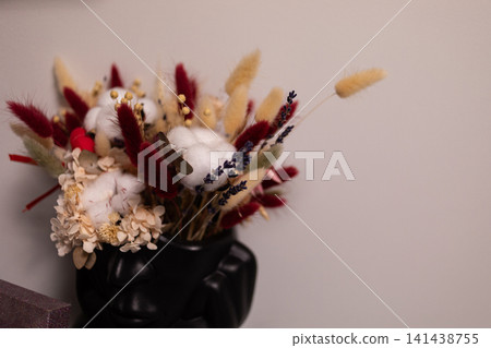 Decorative bouquet of dried flowers and colorful foliage arranged in a glossy black vase against a neutral wall, creating an elegant autumn-inspired home interior accent display Decorative bouquet of dried flowers and colorful foliage arranged in a glossy black vase against a neutral wall, creating an elegant autumn-inspired home interior accent display 141438755
