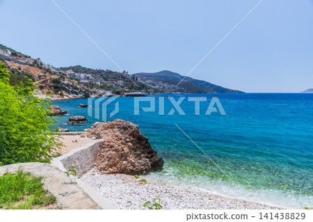 Turquoise waters lap a white pebble beach beneath a rocky coastline Turquoise waters lap a white pebble beach beneath a rocky coastline 141438829