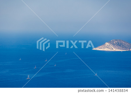Distant boats sail through deep blue sea near a rocky island. Turkey Distant boats sail through deep blue sea near a rocky island. Turkey 141438834
