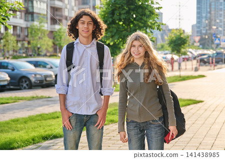Two happy diverse teenager students with backpacks standing outside on a sunny city street Two happy diverse teenager students with backpacks standing outside on a sunny city street 141438985