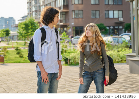 Two happy diverse teen students with backpacks walking and talking outside Two happy diverse teen students with backpacks walking and talking outside 141438986
