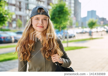Happy teen girl with backpack and backward cap walking outdoors 141438989