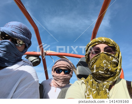 Desert adventure with nomadic travelers three men in traditional headscarves and sunglasses pose on a dune buggy under bright blue sky, capturing the thrill off road exploration in arid landscape. Desert adventure with nomadic travelers three men in traditional headscarves and sunglasses pose on a dune buggy under bright blue sky, capturing the thrill off road exploration in arid landscape. 141439160