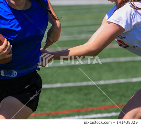 Defender Reaching for the Running backs Flag During a Girls Flag Football Game Defender Reaching for the Running backs Flag During a Girls Flag Football Game 141439329