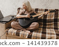 Mature woman practicing guitar beside a laptop at home 141439378