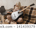 Mature woman using a laptop while holding a guitar at home 141439379