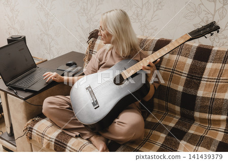 Mature woman using a laptop while holding a guitar at home 141439379
