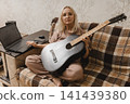Mature woman with guitar using a laptop at home 141439380
