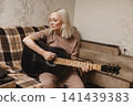 Mature woman playing acoustic guitar in her living room 141439383