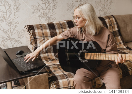 Mature woman practicing guitar with an online lesson Mature woman practicing guitar with an online lesson 141439384