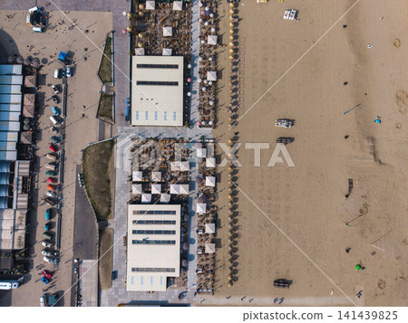 Beautiful top down high altitude aerial panoramic perspective of beach resort clubs with straw parasols white umbrellas vintage cars and paved promenade under bright sunlight Beautiful top down high altitude aerial panoramic perspective of beach resort clubs with straw parasols white umbrellas vintage cars and paved promenade under bright sunlight 141439825