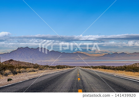 Straight desert road leading toward mountain landscape Straight desert road leading toward mountain landscape 141439920