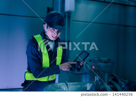 A male worker inspects a rooftop at night using a tablet. Photo courtesy of Denpa Gakuen Educational Foundation, Tokyo Electronics College. 141440256