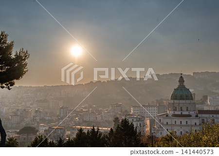 Naples, italy. December 30, 2024. Naples cityscape with the basilica dell'incoronata madre del buon consiglio dome at sunset, soft light through a misty sky Naples, italy. December 30, 2024. Naples cityscape with the basilica dell'incoronata madre del buon consiglio dome at sunset, soft light through a misty sky 141440573