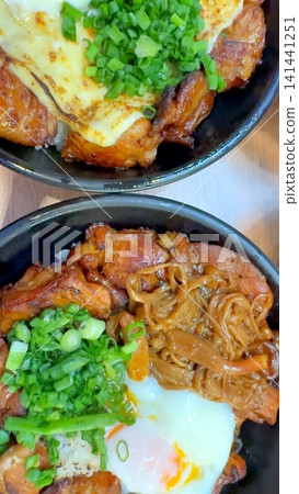 Japanese BBQ rice bowls with grilled chicken, melted cheese, green onions, soft egg, steamed rice, caramelized glaze, and warm savory toppings in closeup overhead view 141441251