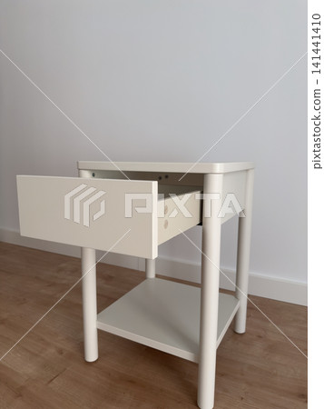 Assembled white nightstand with open drawer against a white wall Assembled white nightstand with open drawer against a white wall 141441410