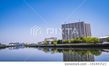 A large apartment building and a blue sky are beautifully reflected on the calm surface of the river. A large apartment building and a blue sky are beautifully reflected on the calm surface of the river. 141441521