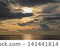 Sunset view of a ship floating on a calm sea, with light filtering through the clouds. 141441814