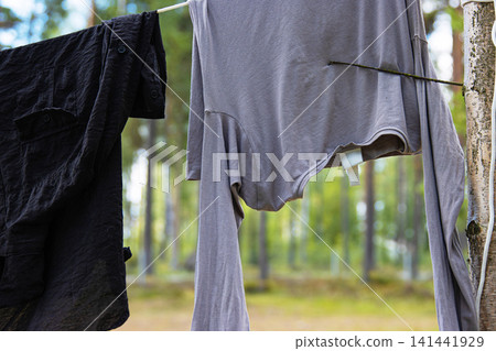 A black and a gray shirt hanging on a line between trees, while air drying in a serene forest in Finland. A black and a gray shirt hanging on a line between trees, while air drying in a serene forest in Finland. 141441929