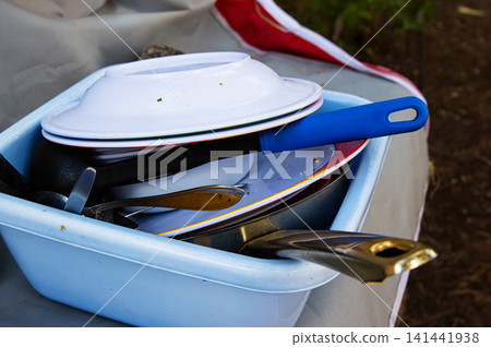 A blue plastic basin full of used dishes, pans, and utensils after a meal at a forest campsite in Finland. 141441938