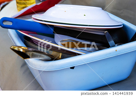 A blue plastic basin full of used dishes, pans, and utensils after a meal at a forest campsite in Finland. A blue plastic basin full of used dishes, pans, and utensils after a meal at a forest campsite in Finland. 141441939