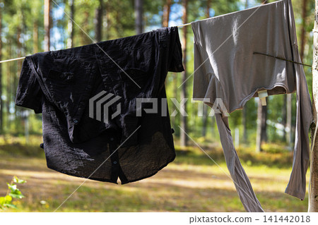 A black and a gray shirt hanging on a line between trees, while air drying in a serene forest in Finland. A black and a gray shirt hanging on a line between trees, while air drying in a serene forest in Finland. 141442018