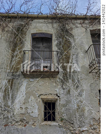 A small barred window sits under an antique balcony on a rough plaster wall. The wall shows signs of age and neglect, reflecting years of wear at a century-old estate. 141442022