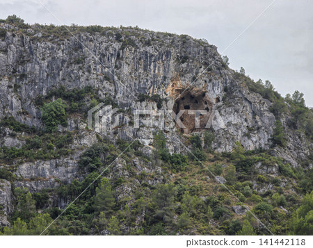 The scene shows a rocky cliff with several natural caves. The cliff is surrounded by green plants typical of the Mediterranean area in Alicante. The scene shows a rocky cliff with several natural caves. The cliff is surrounded by green plants typical of the Mediterranean area in Alicante. 141442118