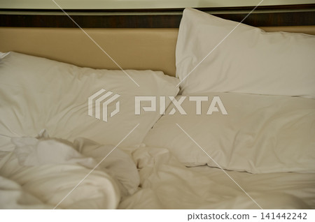 Close-up of the bed with white sheet in the room. Hotel or apartment scene. Close-up of the bed with white sheet in the room. Hotel or apartment scene. 141442242
