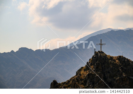 Cross atop mountain peak with layered ridges and soft clouds Cross atop mountain peak with layered ridges and soft clouds 141442510