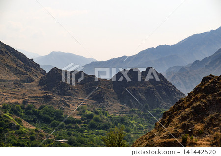 Layered mountain range with green valley below Layered mountain range with green valley below 141442520