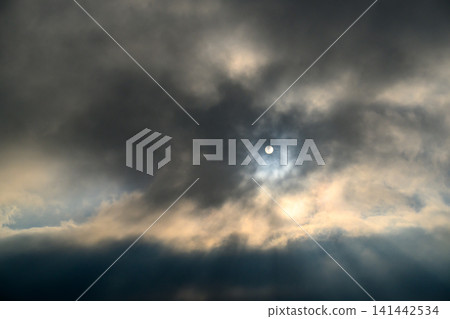 Sunlight breaks through dense clouds around a visible moon 141442534