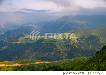 Lush mountain landscape with winding road and distant peaks Lush mountain landscape with winding road and distant peaks 141442535