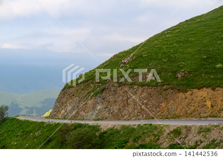 Winding road climbs steep green hillside Winding road climbs steep green hillside 141442536