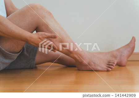 A scene of a man in his 40s sitting on the floor and giving himself a calf massage. A scene of a man in his 40s sitting on the floor and giving himself a calf massage. 141442909