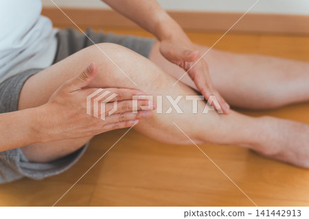 畫面中,一名四十多歲的男子坐在地板上,用雙手為自己按摩腿部。 畫面中,一名四十多歲的男子坐在地板上,用雙手為自己按摩腿部。 141442913