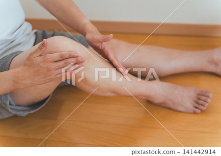 畫面顯示一名 40 多歲的男子坐在地板上，從膝蓋到小腿按摩自己。 141442914