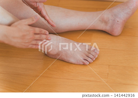 一位四十多歲的男子坐在地板上,為自己按摩腳踝。 一位四十多歲的男子坐在地板上,為自己按摩腳踝。 141442916