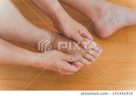 畫面中,一位四十多歲的男子坐在地板上,雙手按摩自己的腳趾。 畫面中,一位四十多歲的男子坐在地板上,雙手按摩自己的腳趾。 141442918