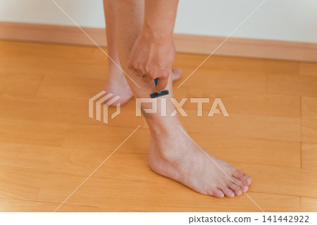 A scene showing a man in his 40s standing and using a razor to shave his leg hair. A scene showing a man in his 40s standing and using a razor to shave his leg hair. 141442922